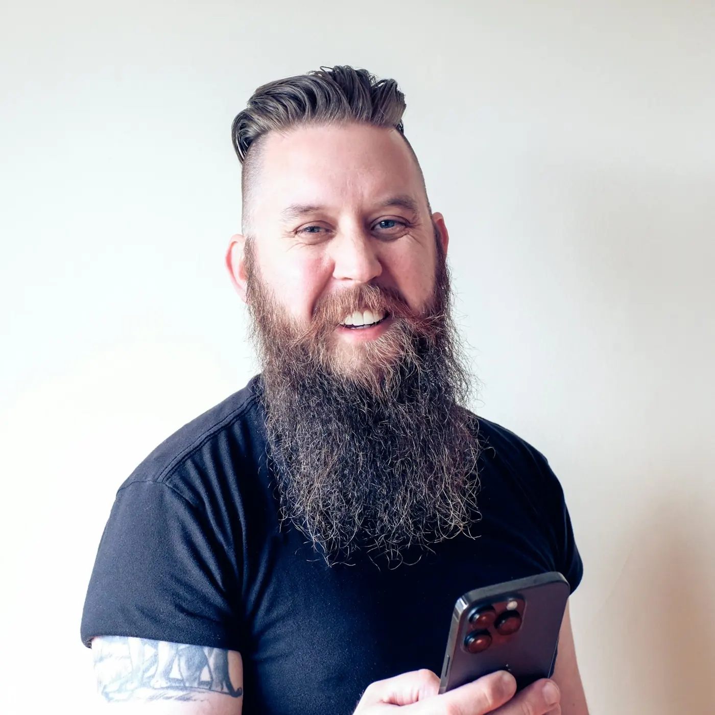 A smiling bearded man holding his phone